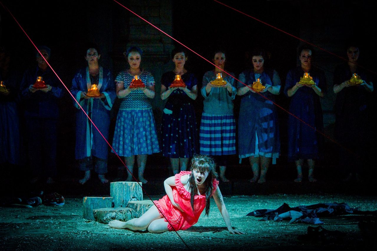 Iris collapsed in red before a line of women holding lanterns