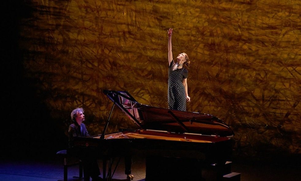 The actress reaching upward behind the piano