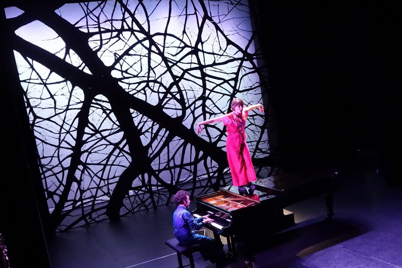 The actress in red above the piano, against a backdrop of branches