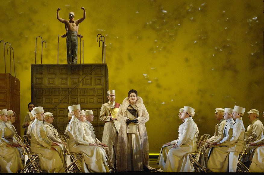 A figure raised above a seated chorus in white