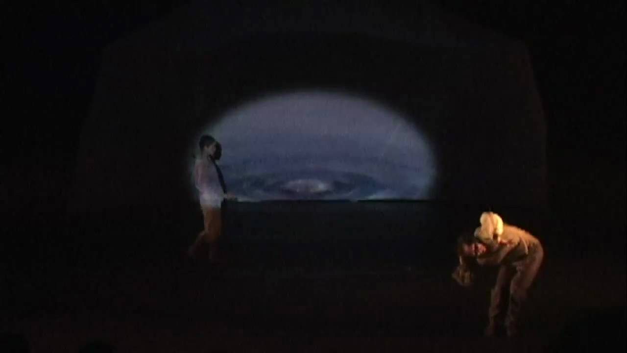 Two dancers in a dark space under a lit oval